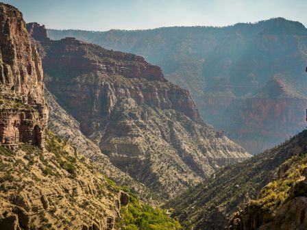 The image shows a stunning view of a rugged canyon with steep cliffs and layered rock formations under a clear sky.