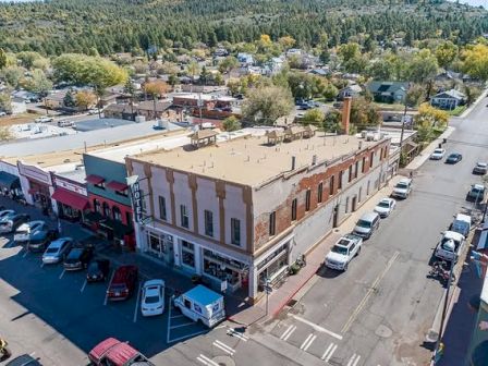 Aerial view of a small town's main street featuring a hotel, various shops, parked cars, and surrounding trees.