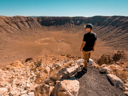 A person stands at the edge of a large crater under a clear blue sky.