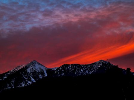 A silhouette of snow-capped mountains beneath a dramatic orange and purple sunset sky.
