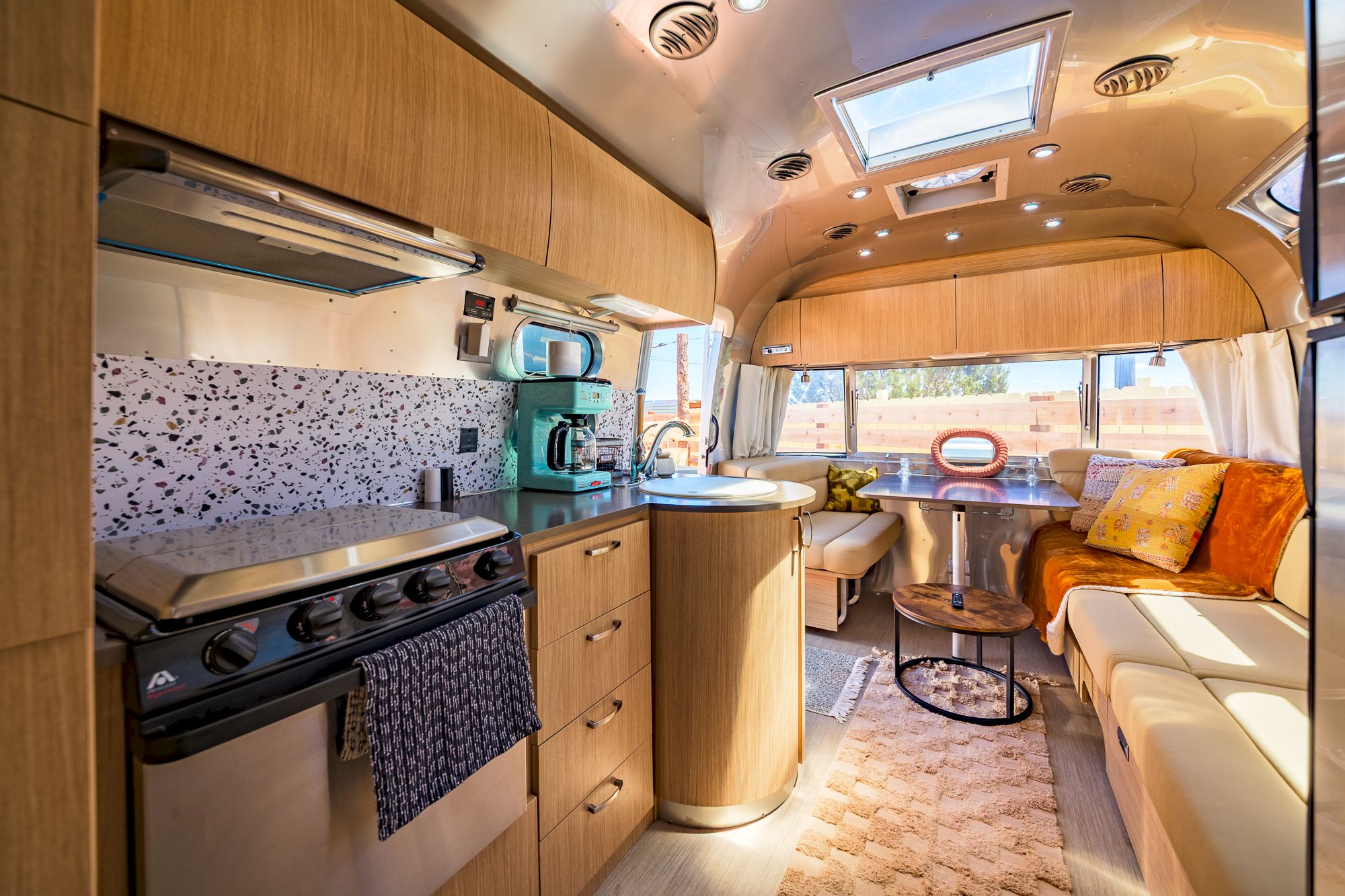 This image shows the interior of an Airstream trailer with a kitchenette, seating area, and stylish decor.