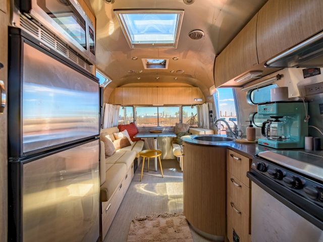 The image shows the interior of a modern RV with a kitchen, seating area, skylight, and windows with a view.