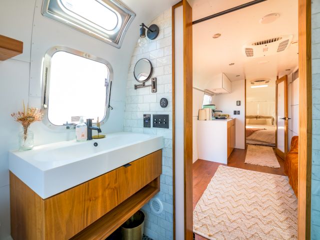 Modern RV interior featuring a bathroom sink and mirror on the left, with a view towards a bedroom at the end of the corridor.