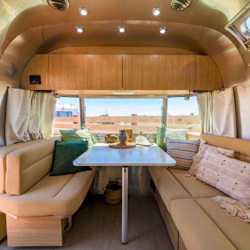 Cozy interior of a camper van with a dining table, seating, cushions, and windows. Bright and inviting atmosphere.