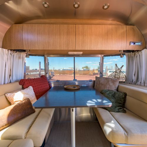 The image shows the interior of a camper van with a table, cushioned seating, and windows revealing an outdoor view.