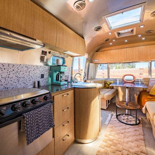 This image shows a cozy RV interior with a kitchenette, seating area, and modern decor.