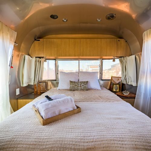 A cozy, well-decorated interior of an RV bedroom with a neatly made bed and folded towels on a tray at the foot.