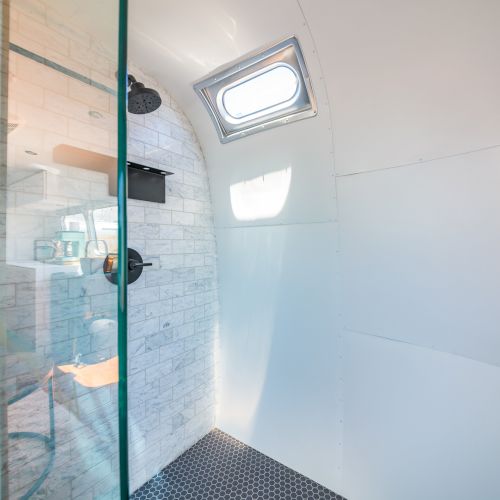The image shows a modern shower with glass doors, a small window, and white walls, part of a sleek bathroom setup.