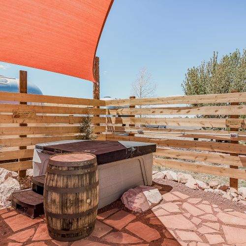 Outdoor space with a wooden hot tub, surrounded by a fence and a shade sail overhead.