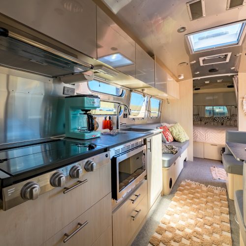 Modern RV interior with a kitchen, dining area, and a bed, featuring wood finishes and skylights for ample natural light in a compact space.