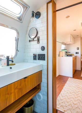 Modern RV interior featuring a bathroom sink and mirror on the left, with a view towards a bedroom at the end of the corridor.